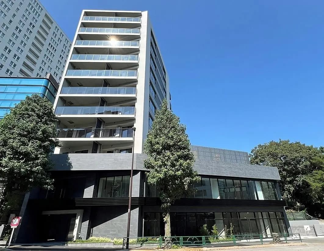 - 都会的なデザインの高層マンション、ガラスバルコニーと緑豊かな木々が映える外観、青空に映える洗練されたスタイル