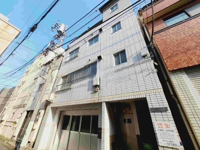 - 都市の狭小住宅の外観、白いタイル貼りの3階建てビルとエントランス、路地と電線が交錯する風景