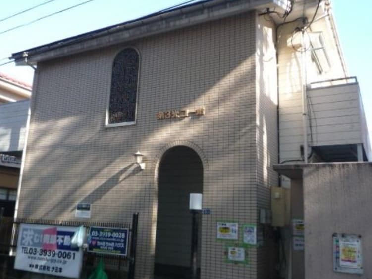- レンガ風の外壁とアーチ型の入口を持つ二階建ての建物、正面に小さな窓と街灯がある住宅風のファサード