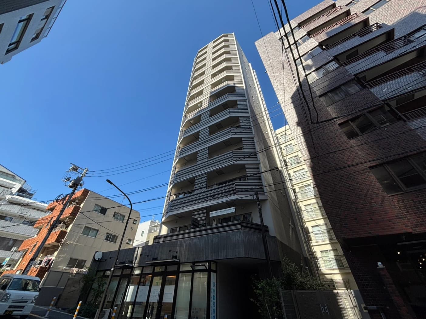 - 高さのある都市のビル群と電線が交差する風景、青空を背景に中央の白い高層マンションが立つ都会的な街並み