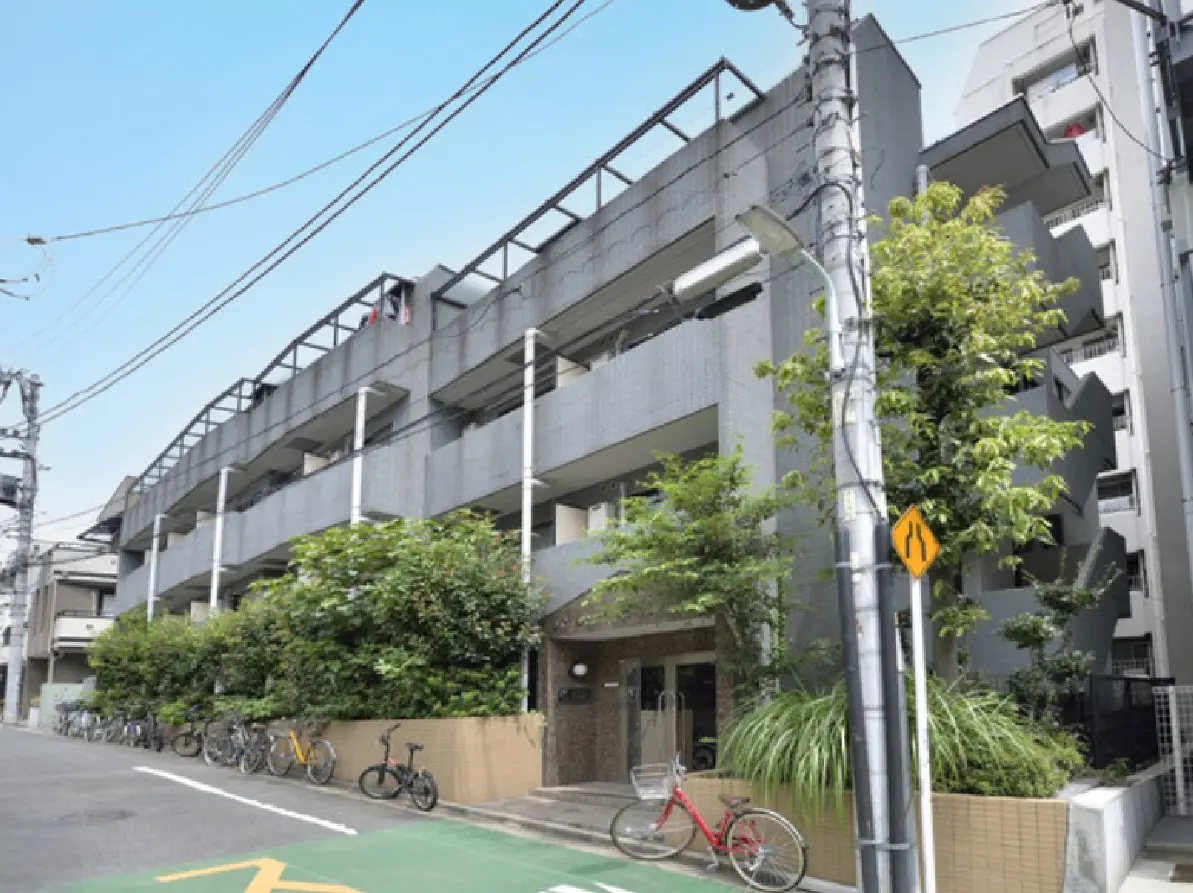 - 自転車が置かれた緑に囲まれた現代的なマンションの外観、周囲に電柱と電線が見える都市の風景