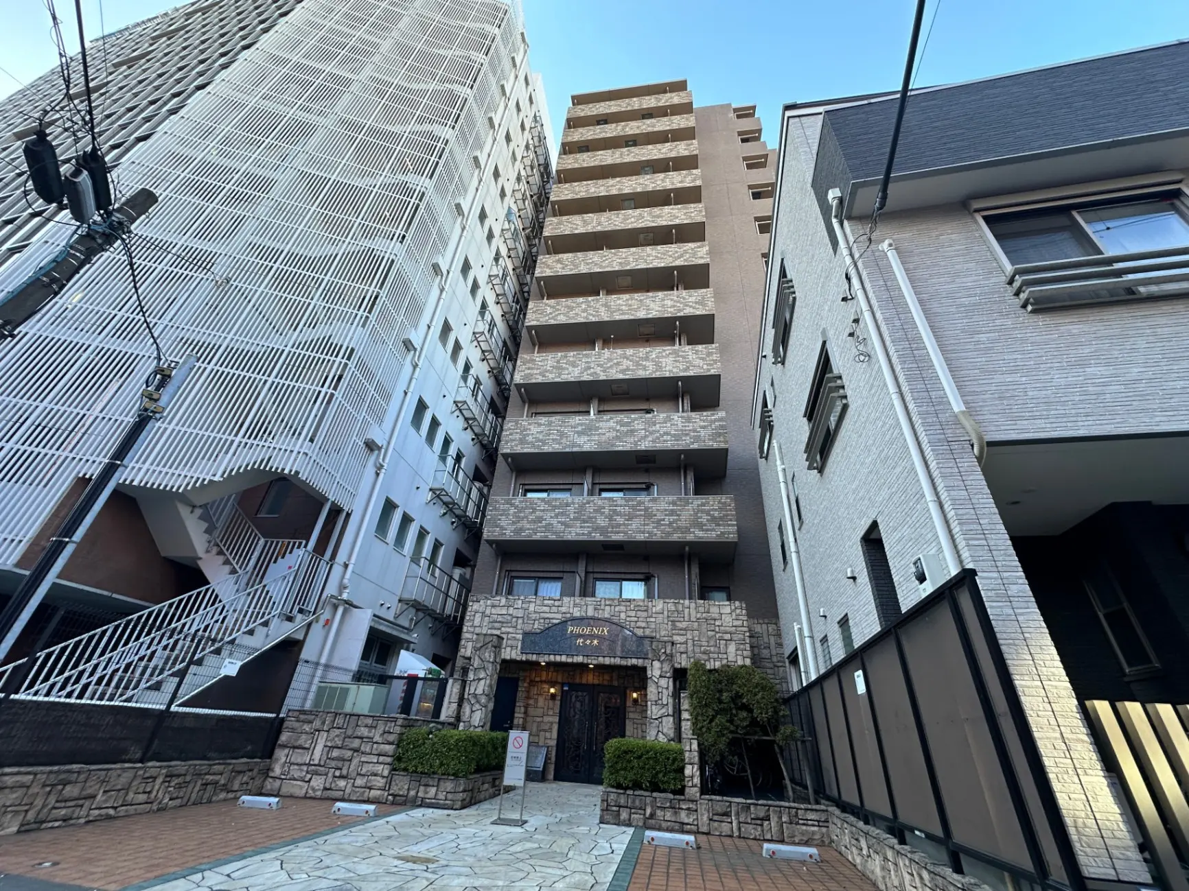 都市のマンションの外観、石造りのエントランスと外階段、晴天のもと近代的な建築デザイン