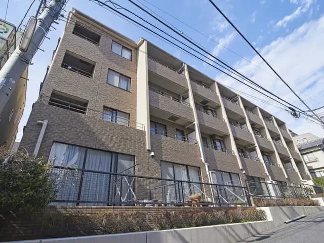 - 低層のブラウンレンガ造りのマンション、バルコニーと大きな窓があり横に並んだ建物の外観、青空が広がる背景