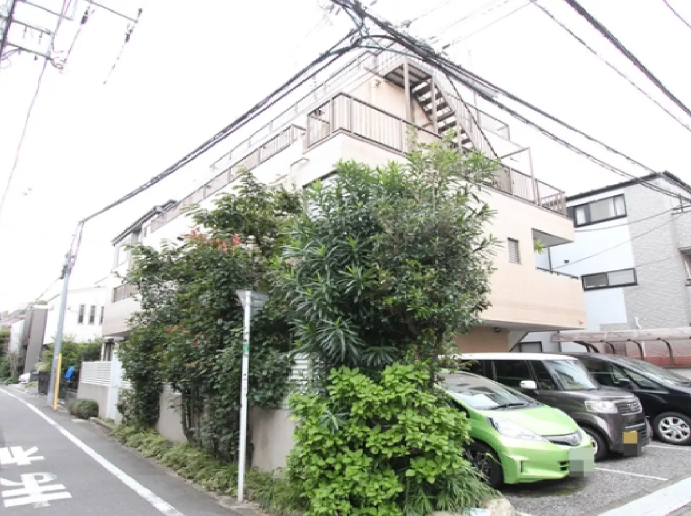 - 緑豊かな植栽に囲まれたアパートの外観、周囲には駐車スペースと歩道が広がる住宅街の風景