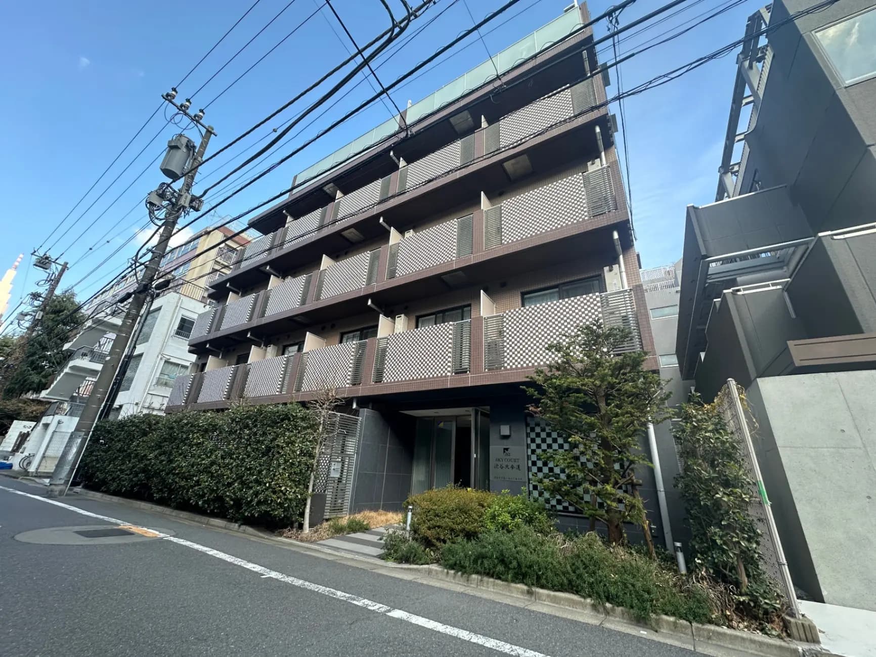 現代的な外観のマンション、茶色の格子模様のバルコニー、緑の植栽がある都市の住宅街