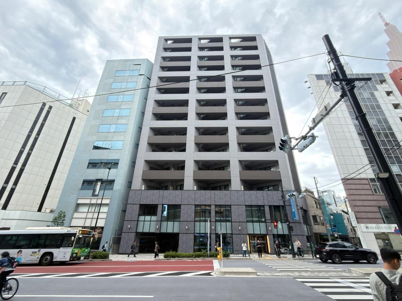 - 都市の高層オフィスビル群、中央の灰色の多階建てビルが左右のビルと交差する交差点に立つ風景