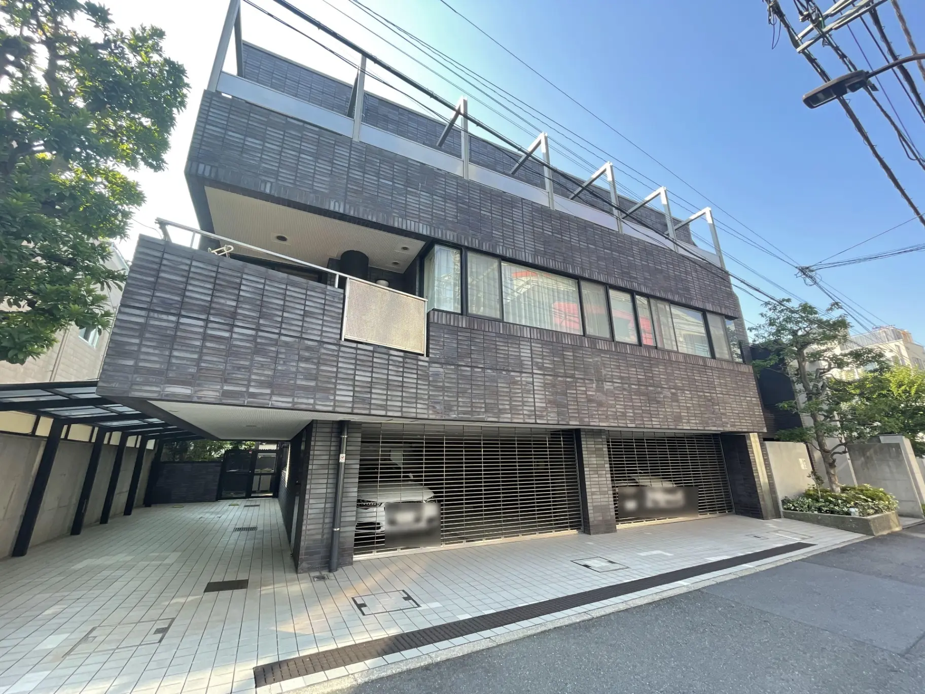 - モダンな外観の3階建て住宅、黒いタイル張りのファサード、大きな窓とバルコニー、車庫付きのエントランス