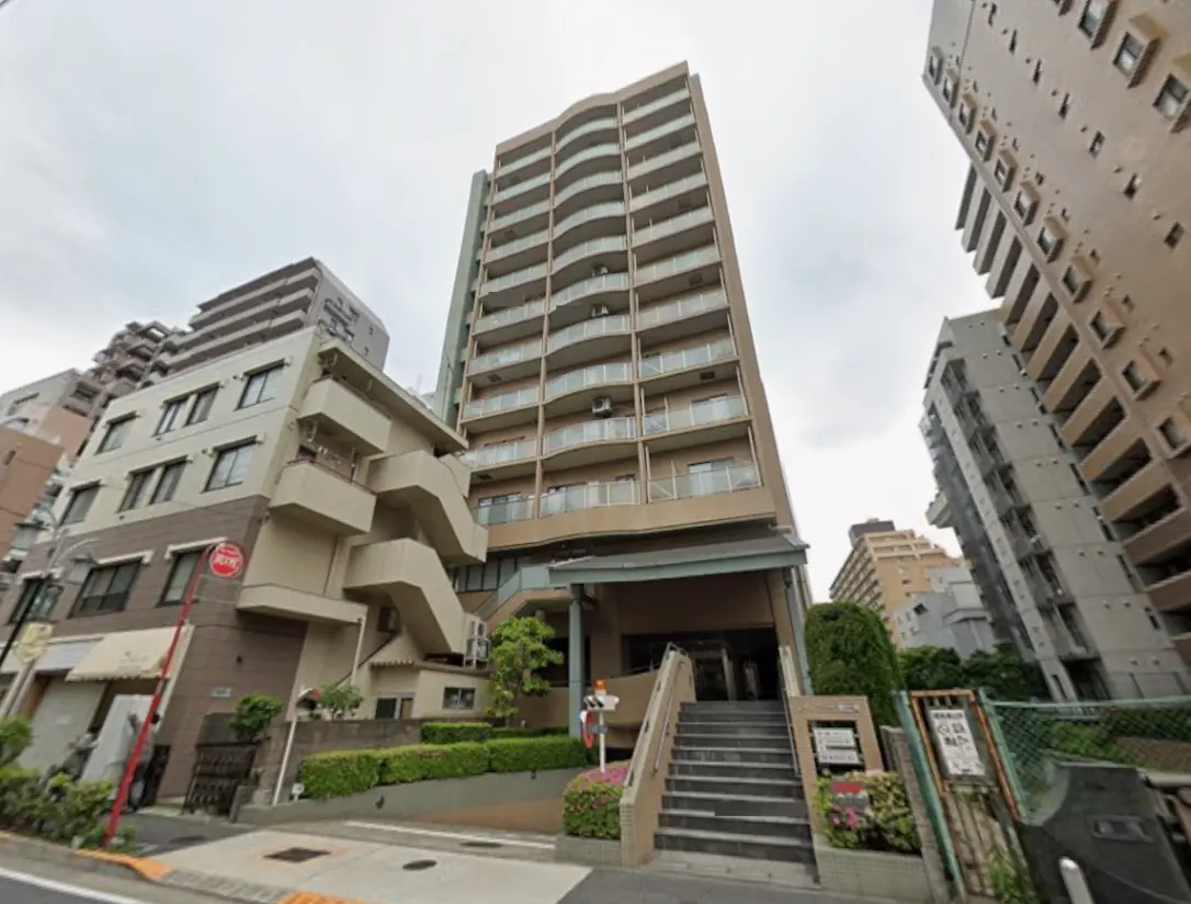 - 都市部に立地する現代的な高層マンション、周囲には他のビルが建ち並び、エントランスには植栽が施された景観