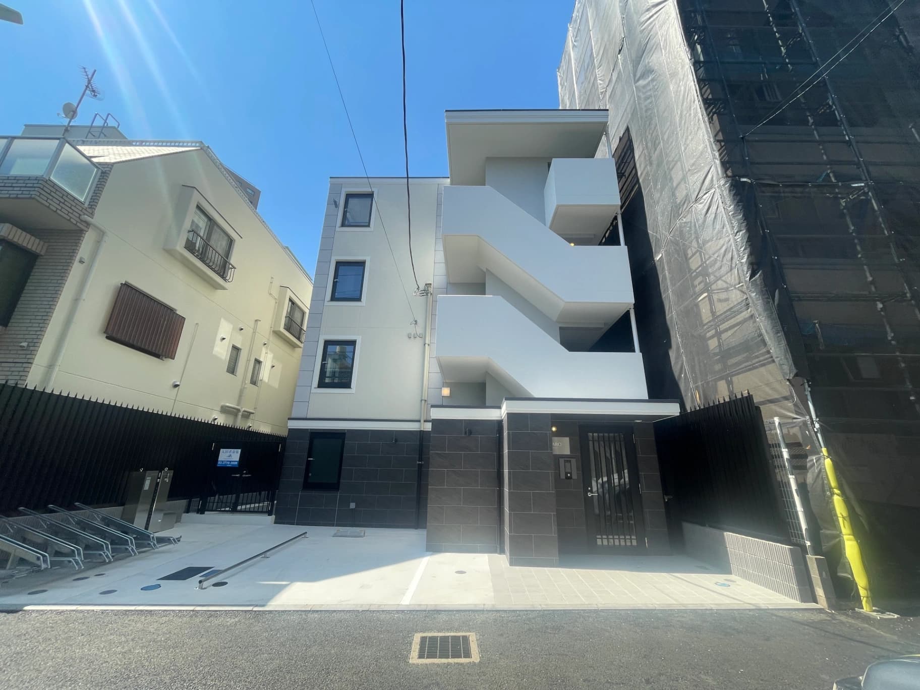 - 白とグレーを基調とした近代的なマンション群、外階段が特徴的な白い建物と隣接するコンクリート造の駐車場エリア
