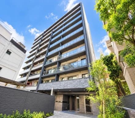 - 都心の高層マンションの外観、黒とグレーの外壁に機能的なバルコニーとエントランス、周囲に緑 leafの植栽と清潔なアプローチ