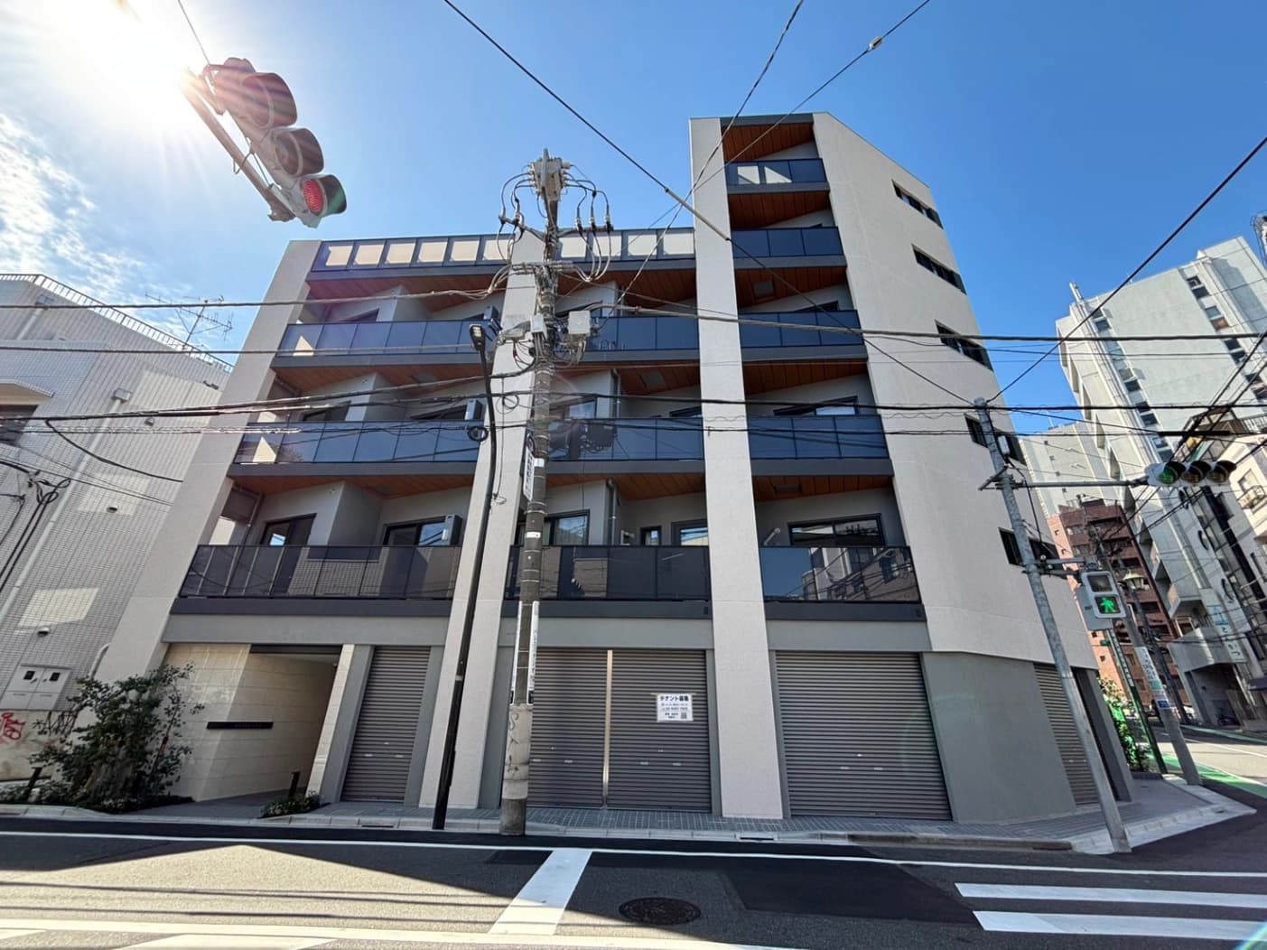 - 都市部の白い多層マンション、ガラス張りのバルコニーとシャッター付きの1階床、電線が交差する街角の風景