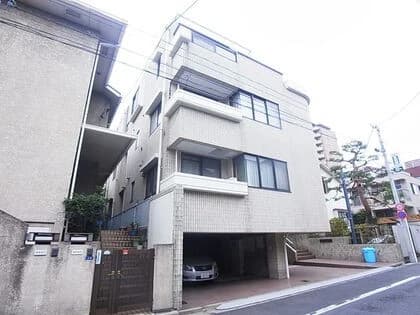 - 都心の三階建て白い外観のマンション、車庫と階段がある連なる建物群、道路沿いの景観