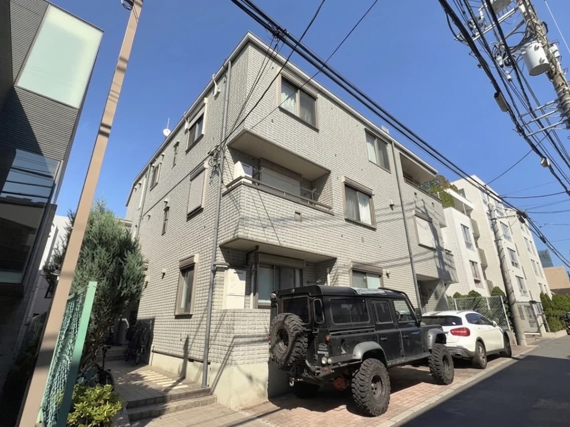 - 都心の角地に建つ白いレンガ調の3階建てマンション、駐車場にはオフロード車と普通車、電線が空に広がる urban street