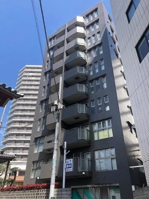 - 高層コンクリート造のスリムなマンション exterior、階段状のバルコニーと大きな窓、周囲に他ビルと電線が映る都市景観