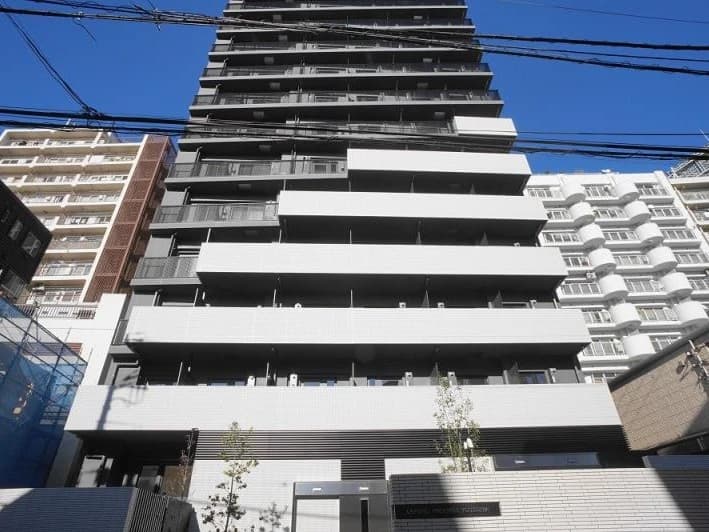 - 高層タワー型の白と黒の exterior が並ぶ現代的なマンション建物、下部にエントランスと小さな植栽