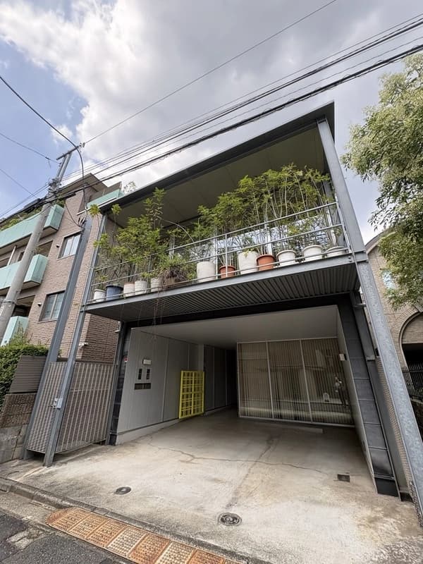 - 都会的な三階建ての住宅外観、ガレージと階段リビングを備えた現代的なデザイン、上部のバルコニーには鉢植えの緑が並ぶ