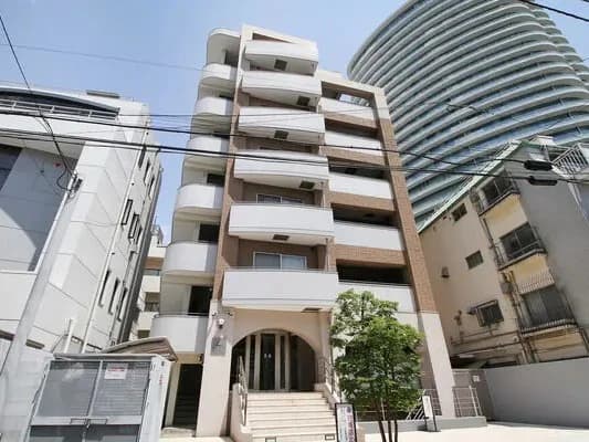 - 都心の高層マンションの正面外観、白とベージュの外壁に curved バルコニー階段状のデザイン、エントランス前の小さな木と階段付きエントランス