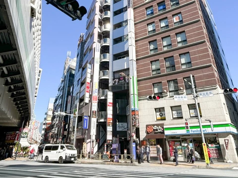 - 路上の交差点と高層ビル群、ファミリーマートなどの店舗が点在する繁華街の風景、 pedestrians and a white vanが通る光景