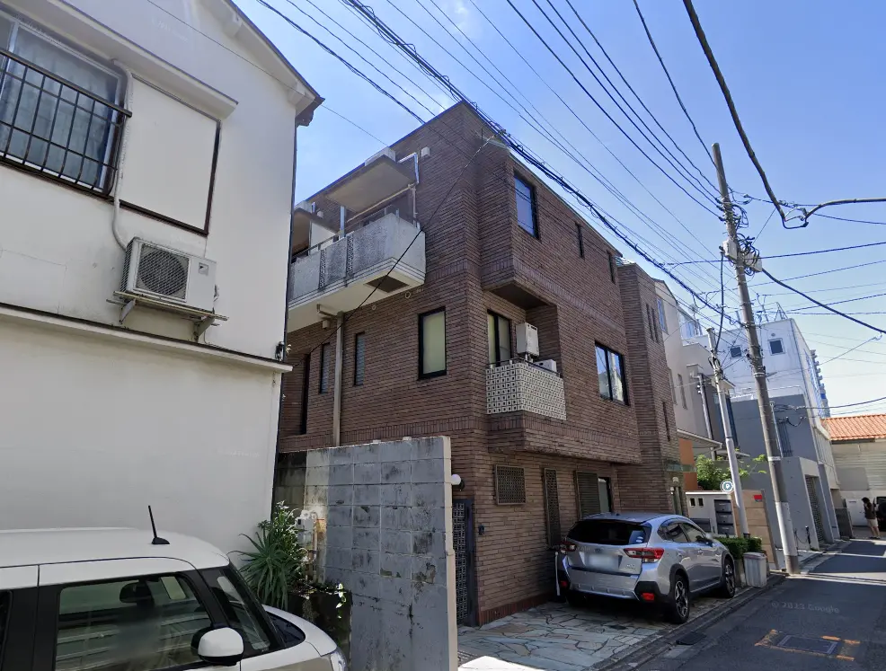 都会の住宅街にあるモダンなレンガ造りのアパートビル、晴れた日の青空と通り沿いの駐車車両