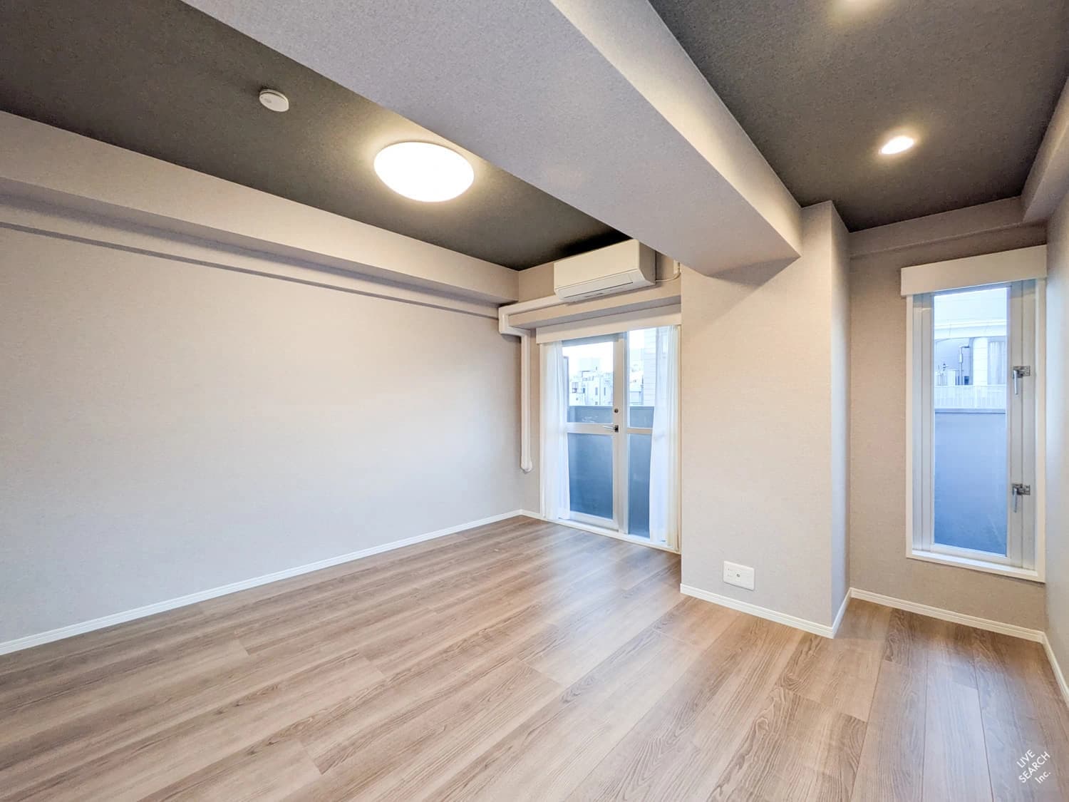 - モダンで明るいリビング風の空間、木目調フローリングと白い壁、窓から自然光が差し込む開放的な室内