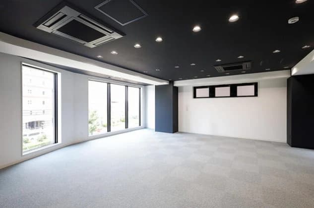 - 開放的なオフィス風フロア、窓際に広がる自然光、モノクロの壁とグレーの床、天井のスポットライトと空調設備が特徴の現代的な内装