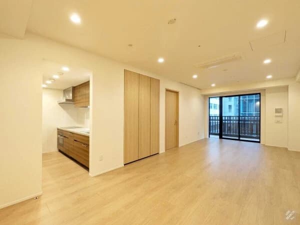 - 明るいリビングダイニングとオープンキッチン、白い壁と木目の扉が並ぶ開放的な居住空間、窓からの自然光とバルコニーが見える室内写真