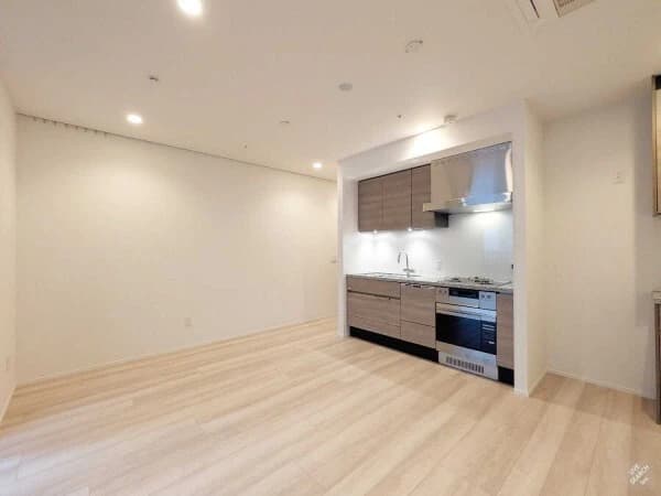 - 開放的なリビングとキッチンが一体化したモダンな空間、木目フローリングと白い壁、シンプルなキッチンキャビネットとIHコンロ付きセミオープンキッチン